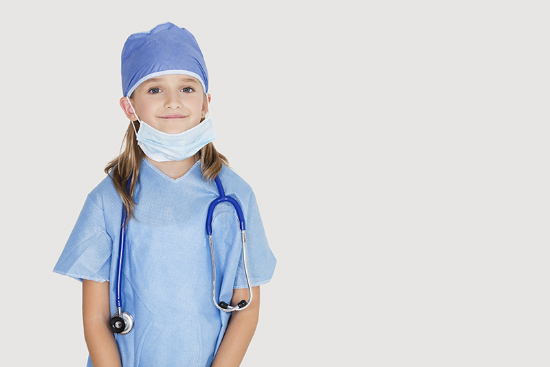 Portrait of young girl in surgeon's costume against gray background
